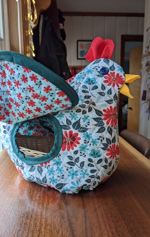 A quilted chicken with its wing raised, showing a hole that leads to the bread basket.